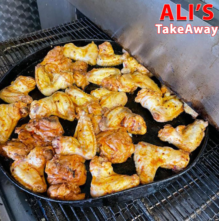 Grilled chicken wings cooking on a hot plate at Ali’s Takeaway in Edinburgh.